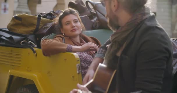 Człowiek uśmiechający się podczas grania muzyki gitarowej z dziewczyną. Kobieta, słuchając chłopak śpiewa piosenki. Kaukaski para w miłości roadtrip wakacje włoskiej podróży na kabriolet vintage car.4k ręczny wideo — Wideo stockowe