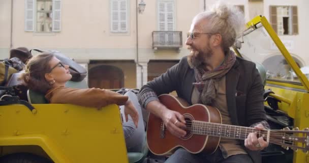 Uomo sorridente mentre suona la musica della chitarra con la ragazza.Donna che ascolta il ragazzo che canta canta.Coppia caucasica innamorata vacanza viaggio in auto italiana convertibile vintage car.4k video palmare — Video Stock