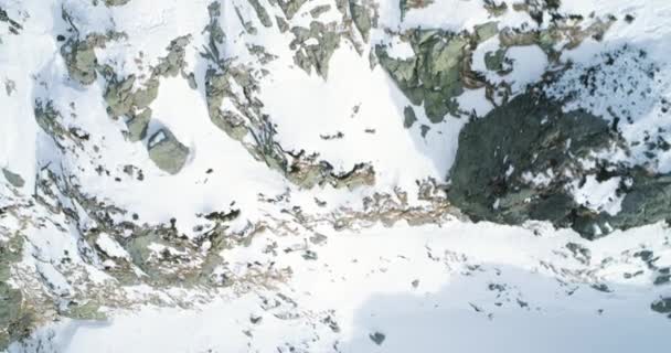 Overhead luchtfoto bovenaanzicht over winter besneeuwde berg stenen. Rocky mountains bedekt met sneeuw en ijs gletsjer. Winter wilde natuur scape buiten establisher.4k drone vlucht straight-down tot oprichting van schot — Stockvideo