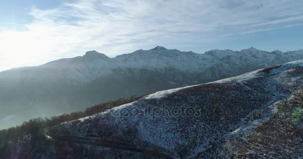 Achterwaartse luchtfoto bovenaanzicht over winter besneeuwde bergweg in zonnige dag. Wit Alpen bergen straat pad sneeuw oprichter met zon shining.4k drone vlucht tot oprichting van schot — Stockvideo