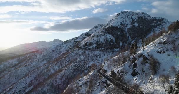 Para a frente vista aérea superior sobre o carro que viaja na estrada na montanha de neve do inverno perto da floresta woods.Snowy montanhas rua caminho estabelecer.Sunset ou nascer do sol backlit.4k voo drone que estabelece tiro — Vídeo de Stock