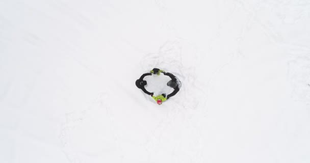 头顶上空的空中俯视着父亲母亲和孩子们在白雪覆盖的冬雪地里围着罗西圈。全家人在一起享受乐趣, 在户外玩得开心. 4 k 直向下透视 — 图库视频影像