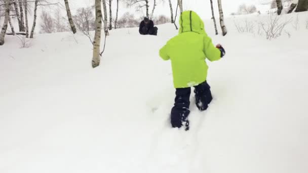 Зима следует за маленьким ребенком, идущим к отцу, играющему со снегом на снежном поле. Семейные люди веселятся вместе за окном. 4k видео — стоковое видео