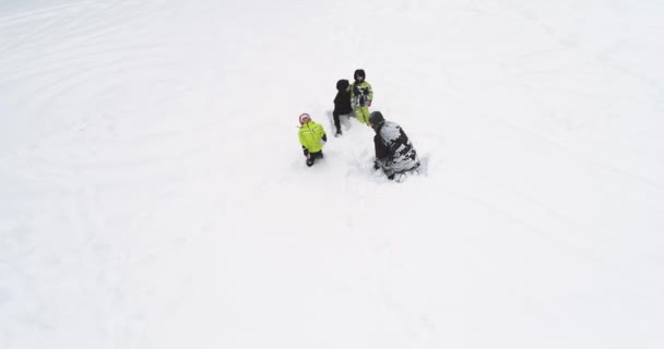 Orbit aerial over father, mother, two children lying playing and hugging on white covered winter snowy field.Family people together enjoy childhood and have fun outdoors.4k straight-down perspective — стоковое видео