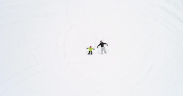 Overhead aerea vista dall'alto su madre e figlia bambino sdraiato facendo angelo della neve su bianco coperto inverno innevato field.Mom e ragazza famiglia persone godono e si divertono outdoors.4k prospettiva dritto verso il basso — Video Stock