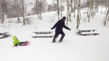 Kış yan babası çocuk ile karlı alan kırmızı kızak çekerek izleyin. Baba, oğlu veya kızı, karda yarış kızağı. Aile insanlar birlikte outdoors.4k video eğlenin