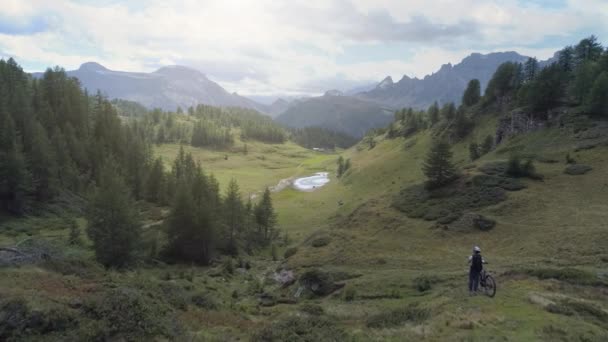 Antena em colinas e bosques florestais com mulher ciclista de montanha olhando panorama paisagem com mtb e-bike no verão ao ar livre.Wanderlust ativa viagem desportiva people.Alps selvagem nature.4k vídeo drone — Vídeo de Stock