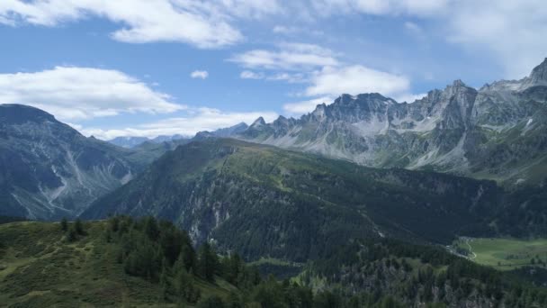 Aérea hacia atrás a bosques de pinos colina del valle alpino de la montaña en verano soleado con nubes. Alpes al aire libre naturaleza verde paisaje montañas vuelo salvaje establishment. — Vídeos de Stock