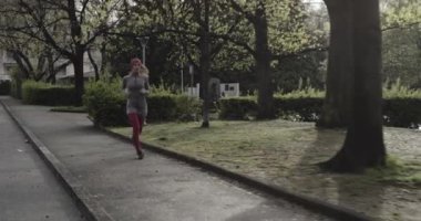 Kadın soğuk mevsimde şehir caddesinde koşuyor ve park ediyor. Kötü hava koşucusu. Şehir parkında kış koşusu. Geriye bakış. Sportif kadın koşuyor..
