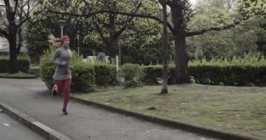 Kadın soğuk mevsimde şehir caddesinde koşuyor ve park ediyor. Kötü hava koşucusu. Şehir parkında kış koşusu. Geriye bakış. Sportif kadın koşuyor..