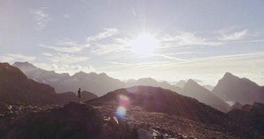 Hava yolu koşucusu adam dağın tepesinde duran hedef ufuk görünümü ne bakıyor.drone atışı. Gün doğumu veya gün batımında açık havada vahşi doğa arkadan aydınlatmalı. Eğitim aktivitesi, spor, çaba, meydan okuma, irade kavramları