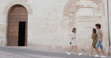 Spello 'nun kırsal kesimindeki bir duvarın yanında yürüyen, gülümseyen ve eğlenen üç mutlu turist arkadaş. Umbria .3k ağır çekimde İtalya gezisi.