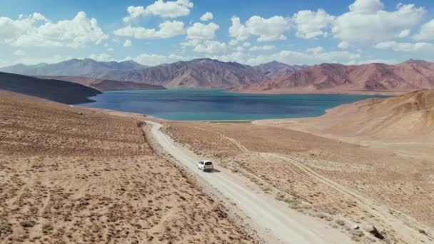 Luftaufnahme eines Geländewagens, der auf einem Schotterweg in Richtung See in den trockenen Bergen.Pamir Highway Seidenstraßenabenteuer in Tadschikistan, Asia.Khorugh Bulunkul See fährt. 4k Drohnenflug-Video — Stockvideo