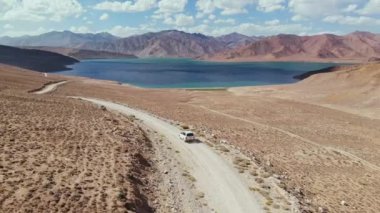 4x4 karayolu üzerindeki hava aracı kurak dağlardaki göl yolunda ilerliyor. Tacikistan, Asya 'da Pamir Karayolu İpek Yolu macerası. Hurugh Bulunkul Gölü. 4k İHA uçuş videosu
