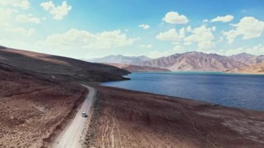 4x4 karayolu üzerindeki hava aracı kurak dağlardaki göl yolunda ilerliyor. Tacikistan, Asya 'da Pamir Karayolu İpek Yolu macerası. Hurugh Bulunkul Gölü. 4k İHA uçuş videosu