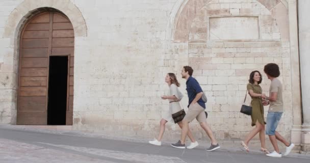 Vier gelukkige toeristen vrienden wandelen, glimlachen en plezier hebben in de buurt van een bakstenen muur in het landelijke stadje Spello.Vrienden Italiaanse reis in Umbrië.4k slow motion — Stockvideo