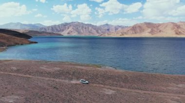 4x4 numaralı yol kenarındaki hava aracı kurak dağlardaki göle doğru çakıl patikası boyunca ilerliyor. Tacikistan, Asya 'da Pamir Otoyolu İpek Yolu macerası. Hurugh Bulunkul Gölü. 4k İHA uçağı