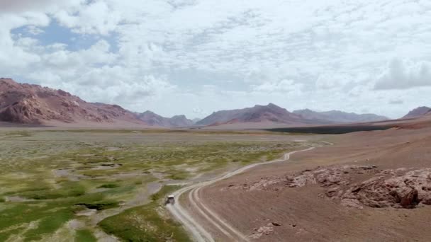 Aerial over off road 4x4 car driving along gravel trail path on arid desert mountains.Pamir Highway silk road trip adventure in Tajikistan desert, Zorkul lake region, Central Asia.4k drone flight video — Video