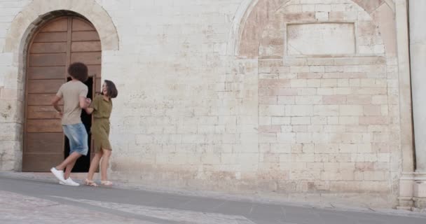 Cuatro personas turísticas felices amigos caminando, sonriendo y divirtiéndose cerca de una pared de ladrillo en la ciudad rural de Spello.Amigos viaje italiano en Umbria.4k cámara lenta — Vídeos de Stock