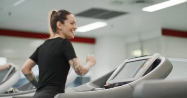 Spor salonunda koşu bandında koşan genç bir kadın. Arkadan bak. Spor salonunda kadın eğitimi. Kardiyo egzersizi yapan kadın.