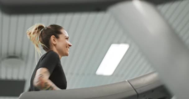 Молода жінка біжить на біговій доріжці в спортзалі. Вид збоку. Навчання жінок у фітнес-центрі. Жінка здійснює кардіо-тренування — стокове відео