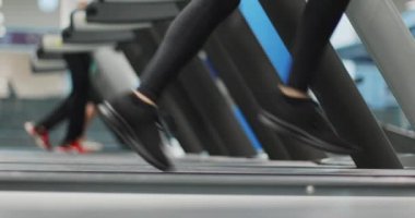 Spor salonunda koşu bandında koşan genç bir kadın. Yan görüş, bacak detayı. Spor salonunda kadın eğitimi. Kardiyo egzersizi yapan kadın.