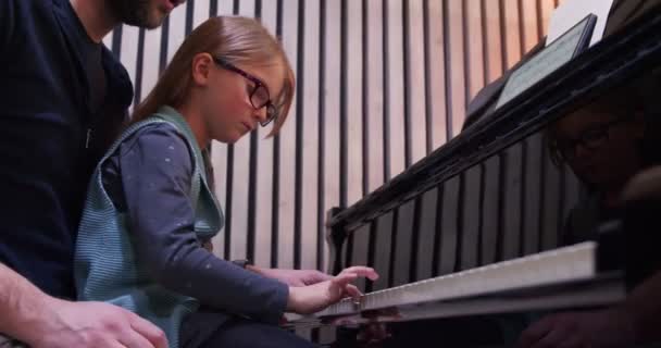 Papà insegna pianoforte alla figlia.Bambina che impara il pianoforte a casa.Vista laterale.Lezione di pianoforte a casa. Bambino che impara il pianoforte da suo padre — Video Stock