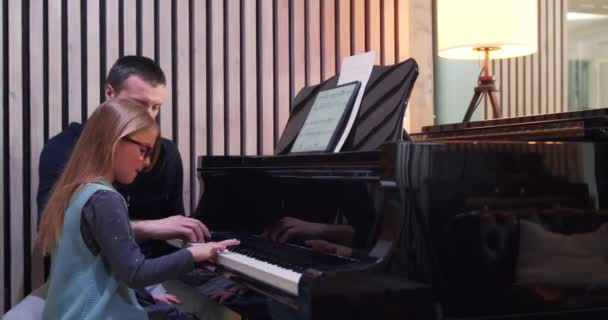 Clase de piano con profesor y niño aprendiendo.Niño aprendiendo a tocar el piano del profesor.Niña aprendiendo lecciones de piano.Vista lateral.Clase de piano en casa. Niño aprendiendo piano de su maestro — Vídeo de stock