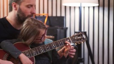 Baba ve kızı birlikte gitar çalıyorlar. Küçük kız evde babasıyla gitar öğreniyor. Ön tarafta gitar dersi.
