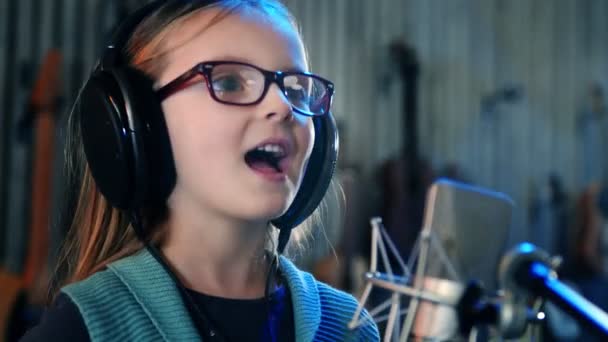 Ragazzina che canta in studio.Bambina che canta una canzone.Vista frontale da vicino. Bambino con le cuffie che frequenta il corso di canto . — Video Stock