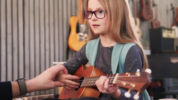 Papà insegna chitarra e ukulele alla figlia.Bambina che impara la chitarra a casa.Close up.Ukulele classe a casa. Bambino che impara la chitarra dal padre — Video Stock