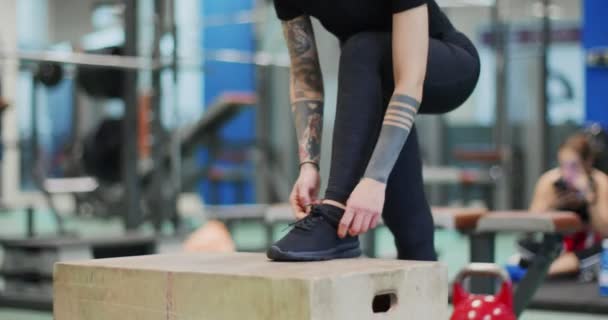 Femme attachant la dentelle sur la boîte de saut à la gymnastique. Préparation de la femme à l'entraînement des jambes en attachant des lacets. Vue de face gros plan, ralenti. Activité cardio fitness. Entraînement de femme au gymnase — Video