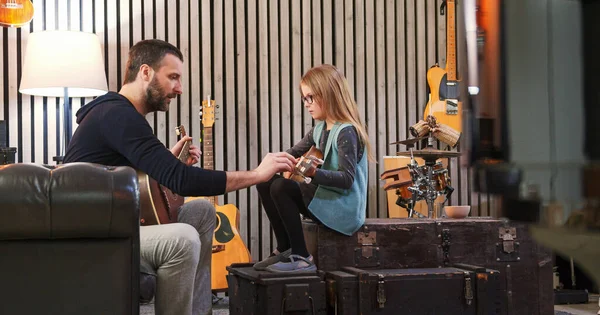 Dad teaching guitar and ukulele to his daughter.Little girl learning guitar at home.Side view.Ukulele class at home. Child learning guitar from her father — Stock Photo, Image