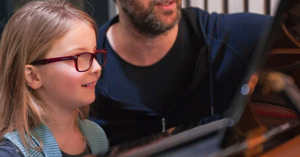 Ragazzina sorridente durante la lezione di pianoforte con l'insegnante.Ragazzina che impara a suonare il pianoforte dall'insegnante.Ragazzina che impara lezione di piano.Vista laterale.Lezione di pianoforte a casa. Bambino che impara il pianoforte dal suo insegnante — Foto Stock