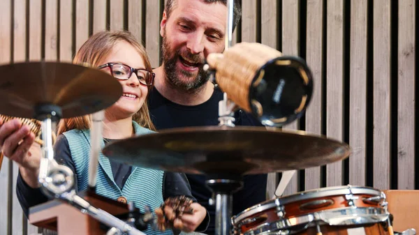 Padre e figlia godono di suonare musica insieme.Bambina sorridente imparare la batteria con il padre a casa.Vista anteriore.Classe di percussione a casa — Foto Stock