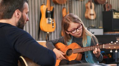 Baba kızına gitar ve ukulele öğretiyor. Küçük kız evde gitar öğreniyor. Ukulele dersini evde kapat. Çocuk babasından gitar öğreniyor.