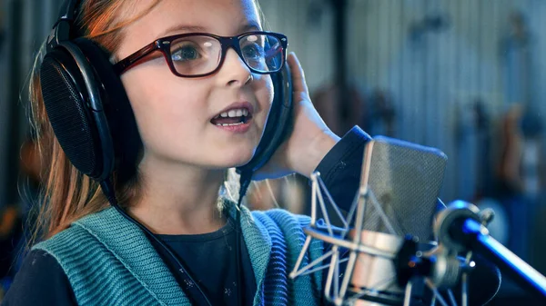 Kind singt im Studio.Kleines Mädchen singt ein Lied.Frontansicht aus nächster Nähe. Kind mit Kopfhörer besucht Singkurs. — Stockfoto