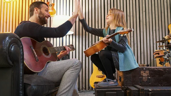 Dad giving five to his daughter celebrating success while teaching music to his daughter.Little girl learning guitar at home.Side view.Ukulele class at home. Child learning guitar from her father