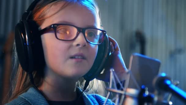 Ragazzina che canta in studio.Bambina che canta una canzone.Vista frontale da vicino. Bambino con le cuffie che frequenta il corso di canto . — Video Stock