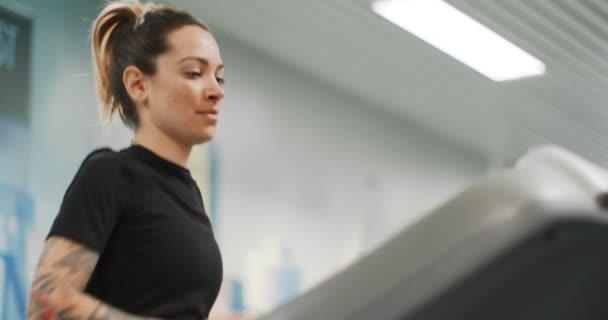 Młoda kobieta biegająca na bieżni na siłowni. Widok z przodu strzał z bliska, górna część ciała. Trening kobiet w centrum fitness. Kobieta ćwiczy cardio workout — Wideo stockowe