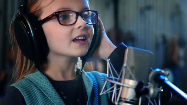 Ragazzina che canta in studio.Bambina che canta una canzone.Vista frontale da vicino. Bambino con le cuffie che frequenta il corso di canto . — Video Stock