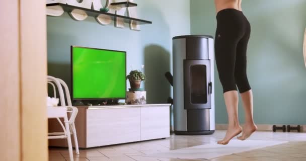 Žena doma cvičí po odlehlé hodině fitness. Žena trénuje doma se zelenou televizí. Jumping Jacks rozcvička. Streaming green screen domestic workout