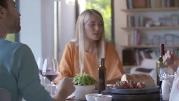 Skupina šťastných přátel mluvit spolu, jíst jídlo, pít víno.Lidé skupina těšit moderní domácí party večeře nebo oběd.Handheld video — Stock video
