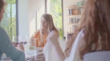 Bir grup mutlu arkadaş sohbet ediyor, yemek yiyor, şarap içiyor. İnsanlar modern ev partilerinin ya da öğle yemeğinin tadını çıkarıyor.