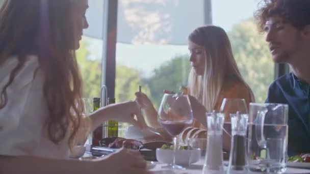 Skupina šťastných přátel mluvit spolu, jíst jídlo, pít víno.Lidé skupina těšit moderní domácí party večeře nebo oběd.Handheld video — Stock video