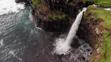 Uçurum manzarasından çarpıcı bir şelale fışkırıyor. Faroe Adaları 'ndaki Gasadalur Köyü yakınlarında Mulafossur şelalesi. Havadan çekim, gün ışığı, bulutlu hava