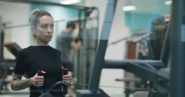 Kadın spor salonunda kürek çekme makinesiyle egzersiz yapıyor. Ön görüş, yavaş çekim. Kürek makinesinde kadın eğitimi