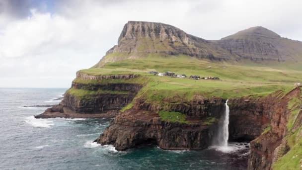 Uçurum manzarasından çarpıcı bir şelale fışkırıyor. Faroe Adaları 'ndaki Gasadalur Köyü yakınlarında Mulafossur şelalesi. İleriye dönük çekim, gün ışığı, bulutlu hava — Stok video