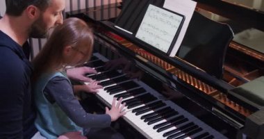 Babası kızına piyano öğretiyor. Küçük kız evde piyano öğreniyor. Evde piyano dersi. Çocuk babasından piyano öğreniyor.