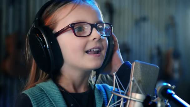 Ragazzina che canta in studio.Bambina che canta una canzone.Vista frontale da vicino. Bambino con le cuffie che frequenta il corso di canto . — Video Stock